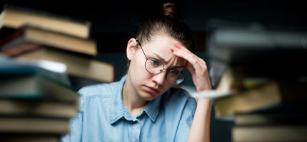 A young person looking stressed while surrounded by books