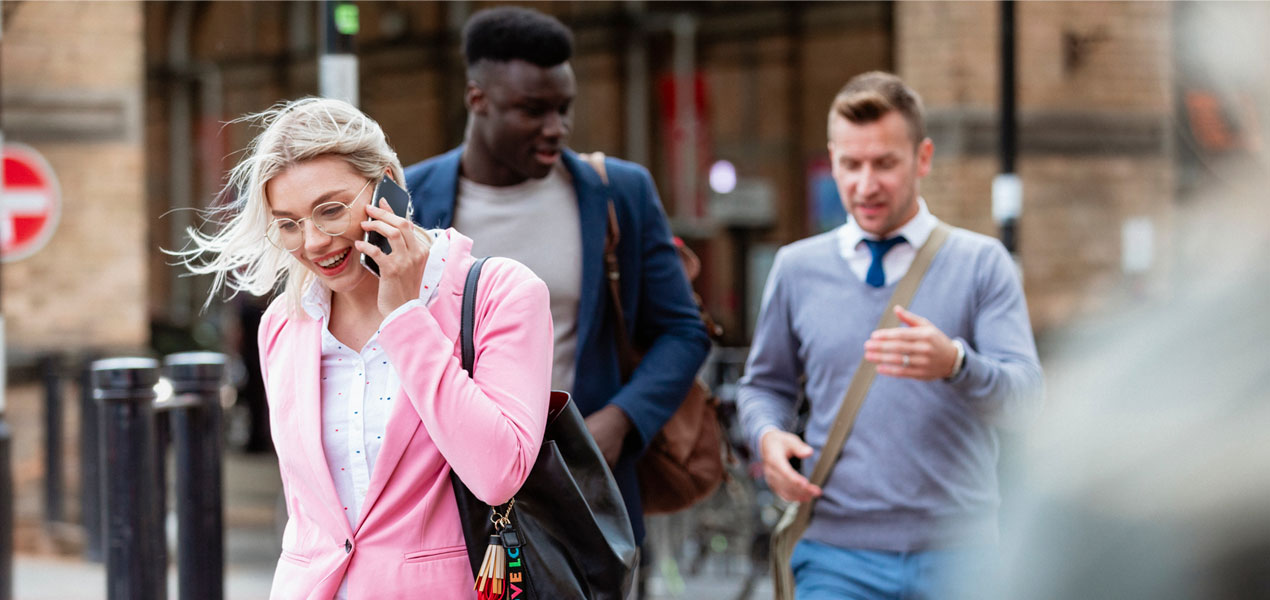 A business woman in a pink suit talking on the phone while crossing the street.