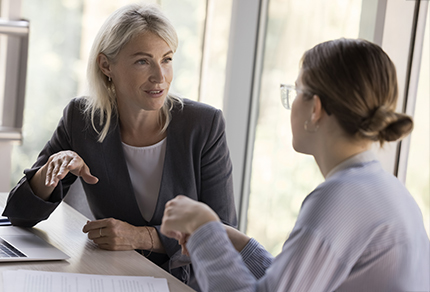 An experienced professional woman looking at and speaking with a younger professional.