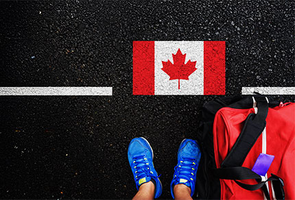 An arial view of a person standing on a street with a Canadian flag and a duffle bag at their feet.