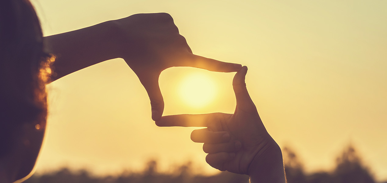 A person framing the sun with their thumb and forefinger.