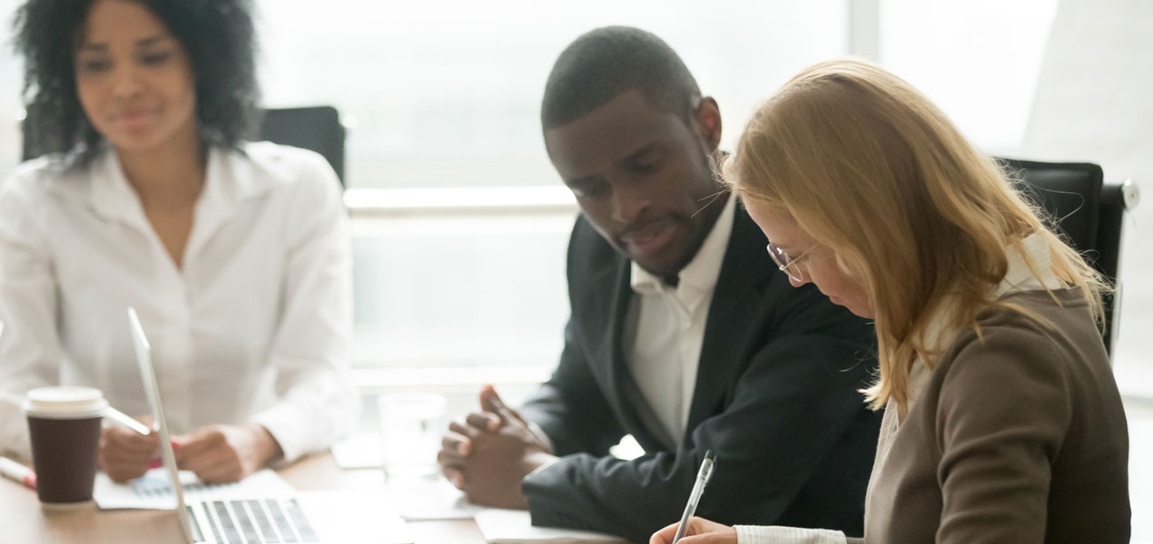 Three business people sat at a meeting table with one woman signing documents.