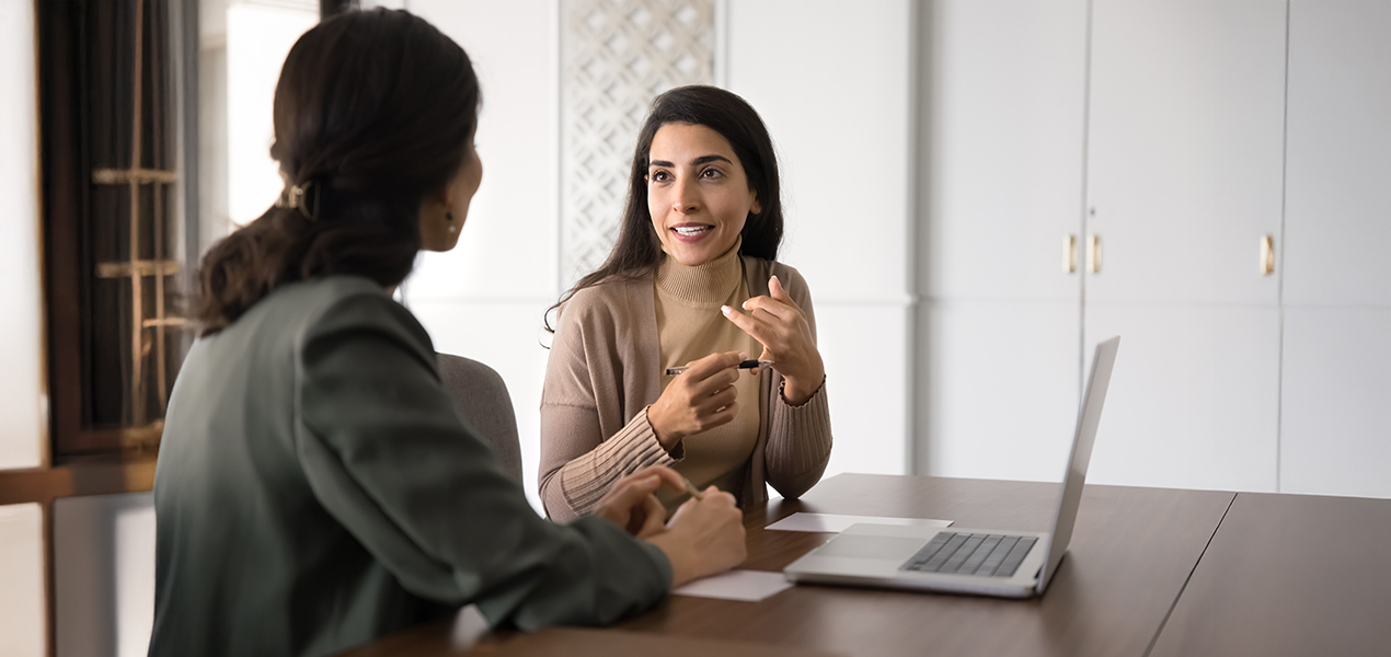 Two professional women in discussion while sitting at a table.