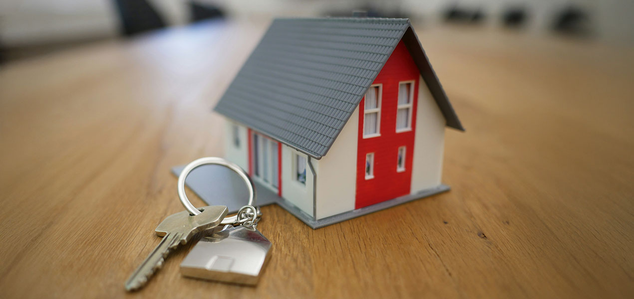 A small house on a desk with a set of keys.