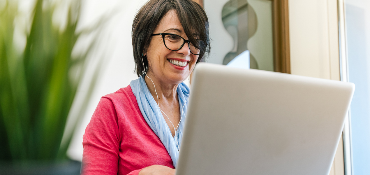 Mature woman wearing a headset, working on laptop.