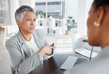 A business woman pointing to a document on a tablet to another person.
