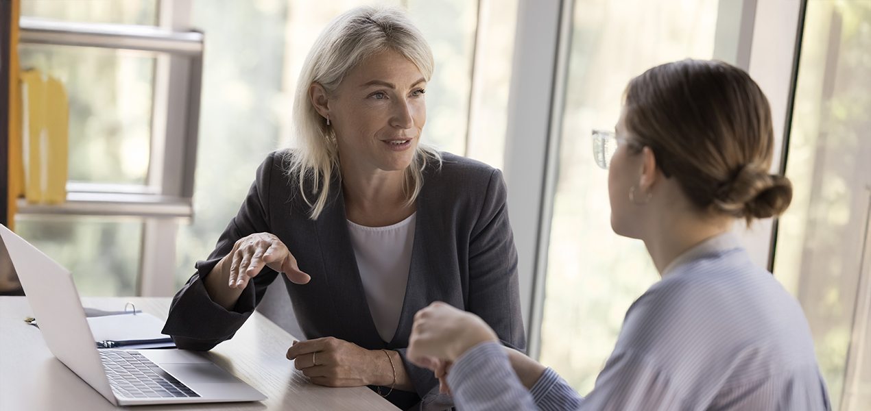 An experienced professional woman looking at and speaking with a younger professional.