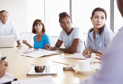 People sitting around a meeting table and looking towards a colleague at the end of the table.