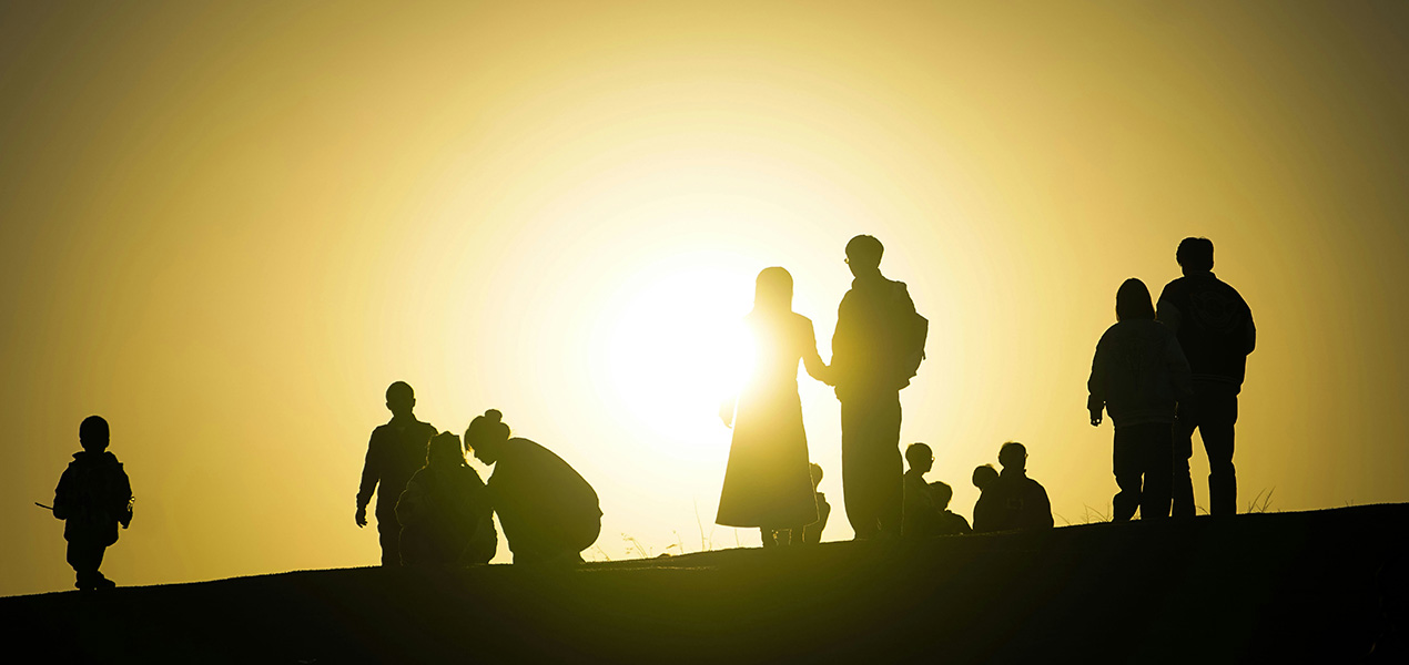 A group of people standing on a hill backlit by the sun. 
