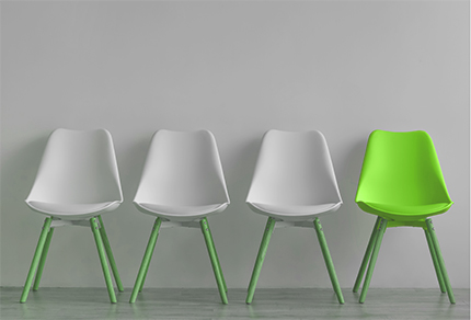 Three empty white chairs and one green chair sitting against a wall.