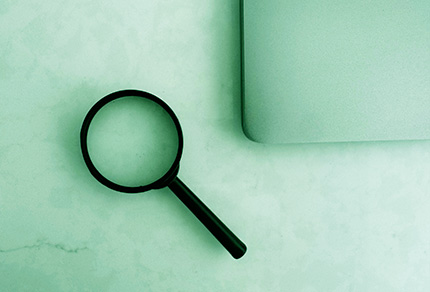 A magnifying glass and a laptop on a table.