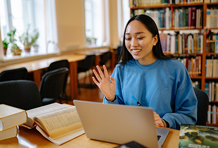 A young student surrounded by books starting a zoom meeting on a laptop.