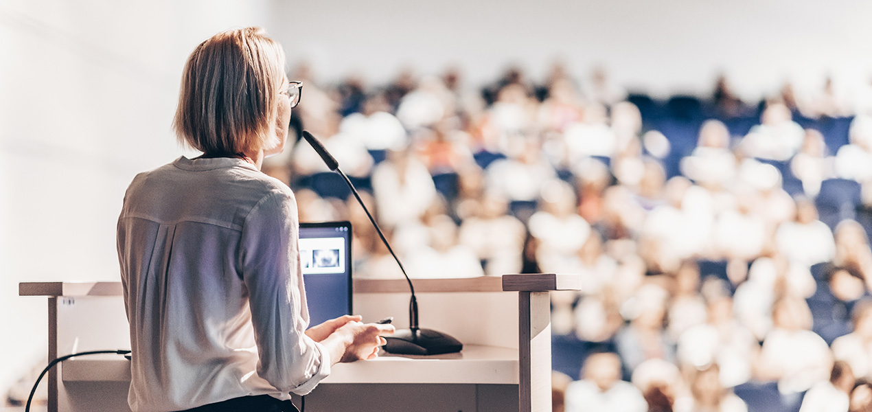A woman standing at a podium speaking to a large audience.
