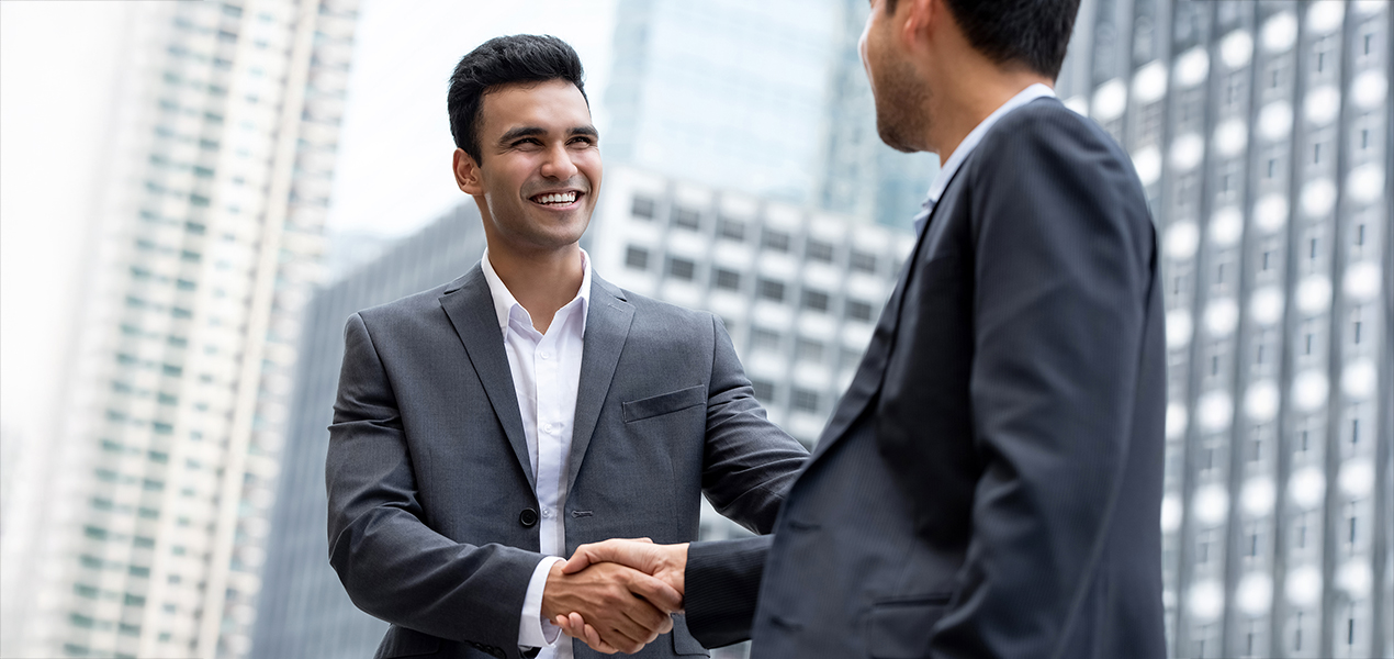 A young professional man in a suit shaking hands with another man in a suit.