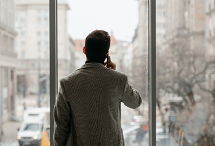 A man talking on a phone looking out the window of his office.