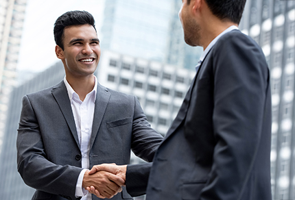A young professional man in a suit shaking hands with another man in a suit.