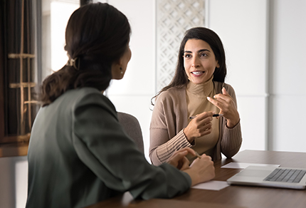 Two professional women in discussion while sitting at a table.