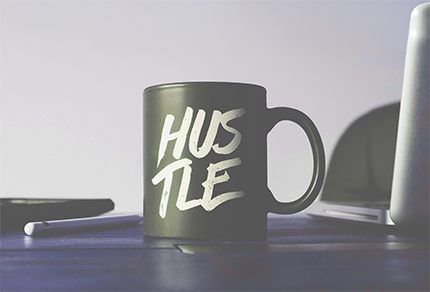 A mug with the word "Hustle" on it sitting on an office desk.