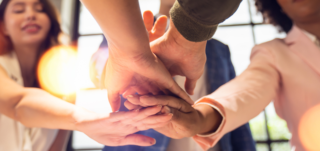 A group of people stack their hands together in a gesture of teamwork.