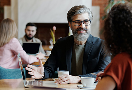 A middle-aged person talking with another person over coffee.