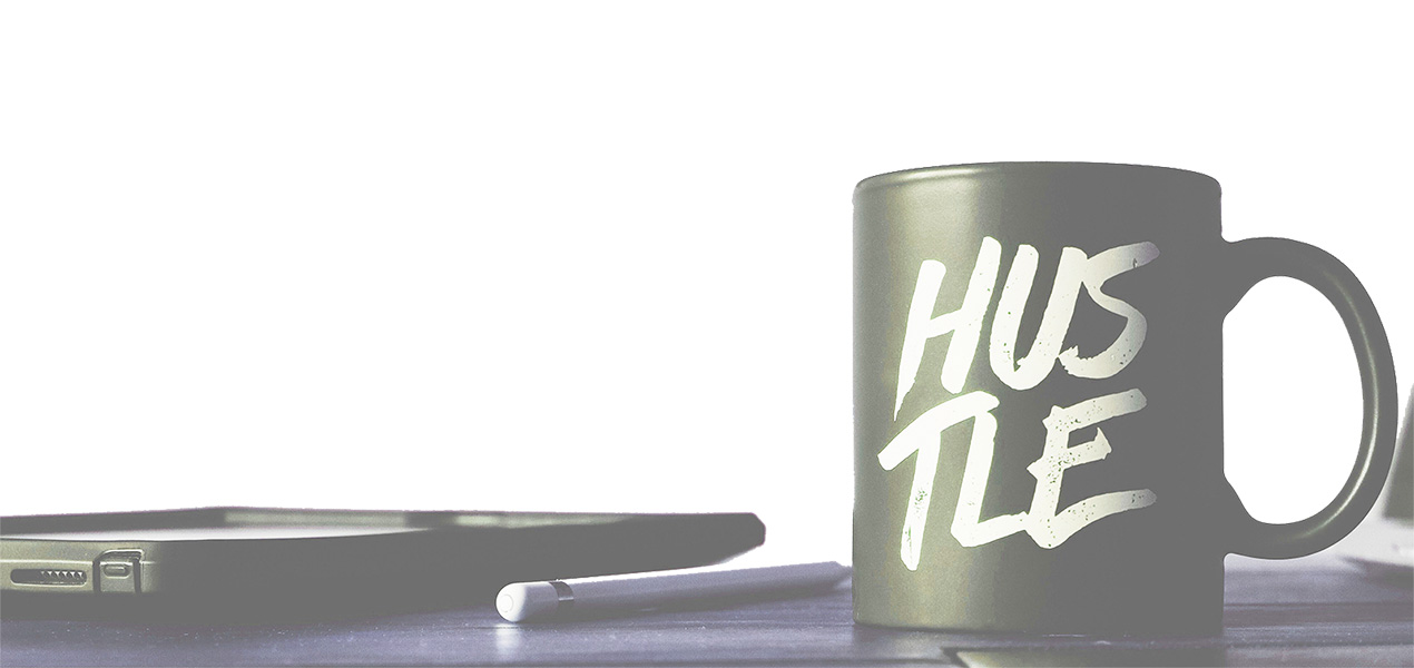 A mug with the word "Hustle" on it sitting on an office desk.