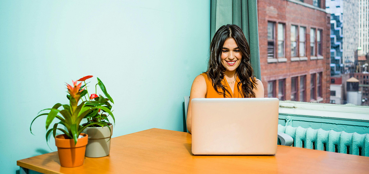 A young woman sitting at a table looking at her laptop.