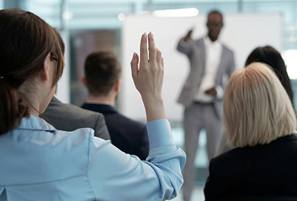 In a large audience, a female participant raises her hand.