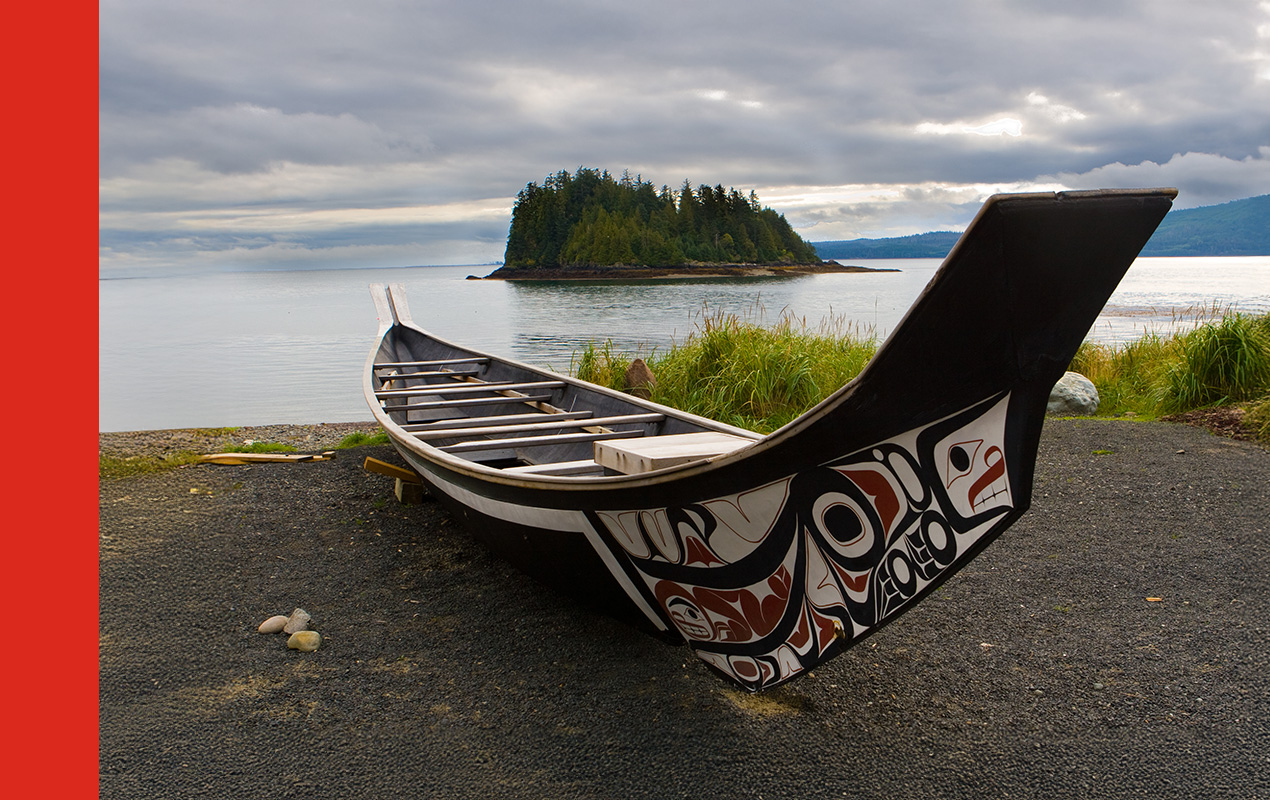 An Indigenous painted canoe resting on the shore of the ocean.