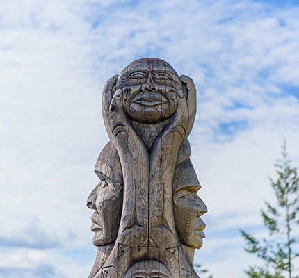 The top of a wood totem with two faces looking left and right with another face above it.
