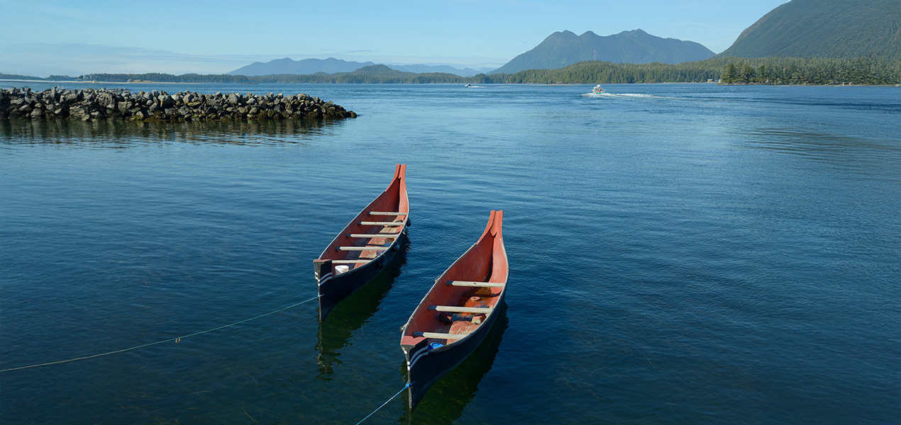 Two Indigenous canoes resting on the shore of the Pacific Ocean.